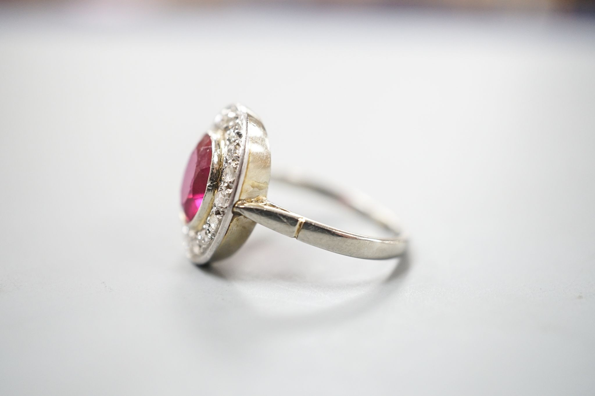 A white metal, synthetic ruby and diamond set oval cluster ring, size N, gross weight 3.4 rams.